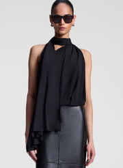 Woman wearing a black sleeveless top with a draped design and a leather skirt on a white background