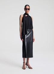 Woman wearing a black sleeveless top with a draped design and a leather skirt on a white background