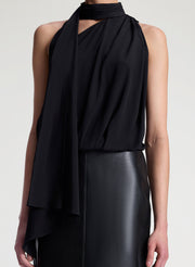 Woman wearing a black sleeveless top with a draped design and a leather skirt on a white background