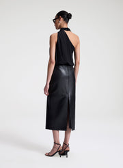 Woman wearing a black sleeveless top with a draped design and a leather skirt on a white background