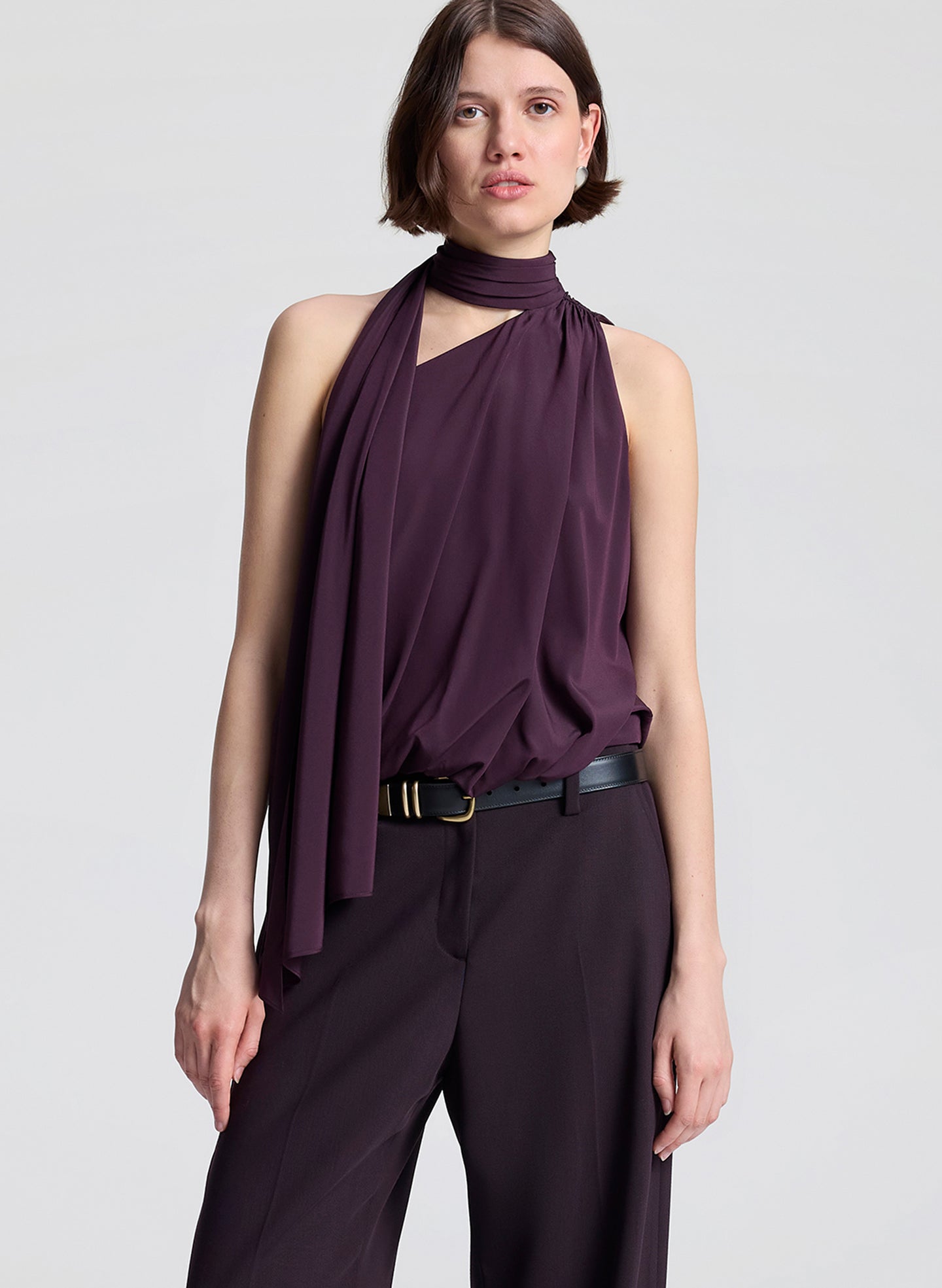 Woman wearing a purple sleeveless top and dark purple pants on a light gray background