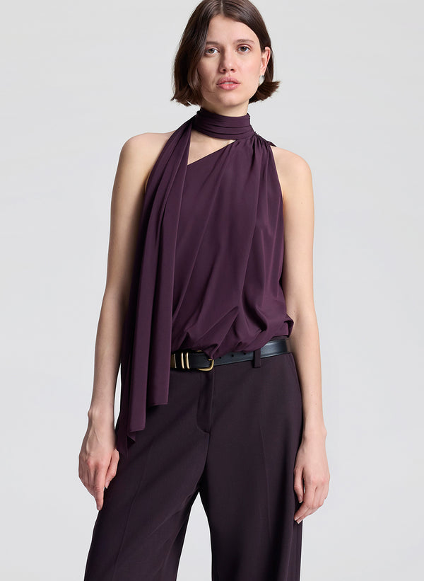 Woman wearing a purple sleeveless top and dark purple pants on a light gray background