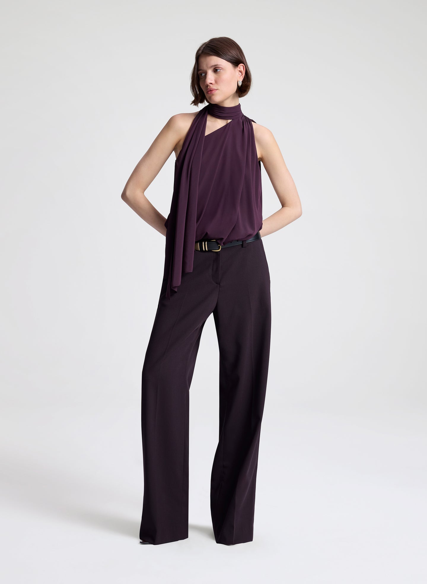 Woman wearing a purple sleeveless top and dark purple pants on a light gray background