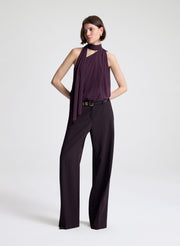 Woman wearing a purple sleeveless top and dark purple pants on a light gray background