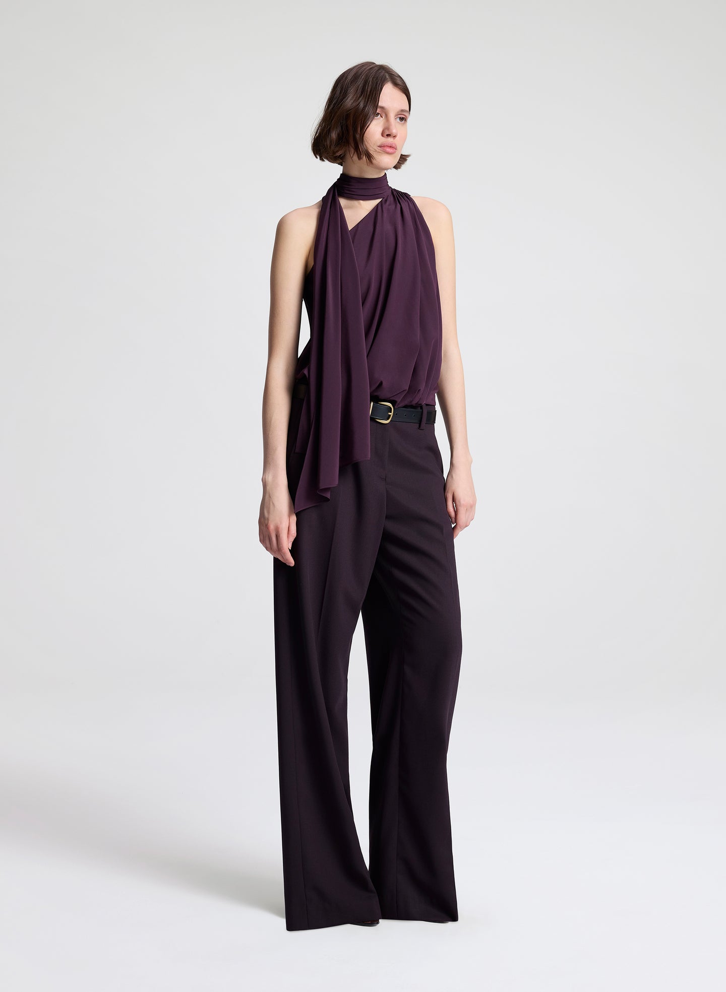 Woman wearing a purple sleeveless top and dark purple pants on a light gray background