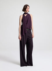 Woman wearing a purple sleeveless top and dark purple pants on a light gray background