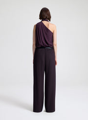 Woman wearing a purple sleeveless top and dark purple pants on a light gray background