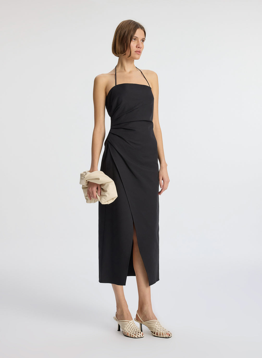 side view of woman wearing black halter neckline ruched midi dress