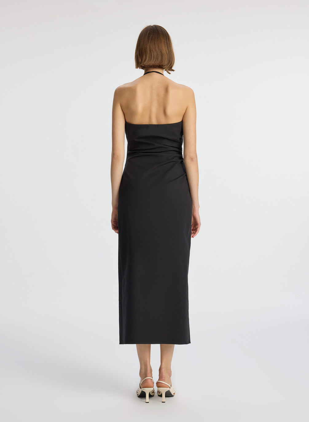 back view of woman wearing black halter neckline ruched midi dress