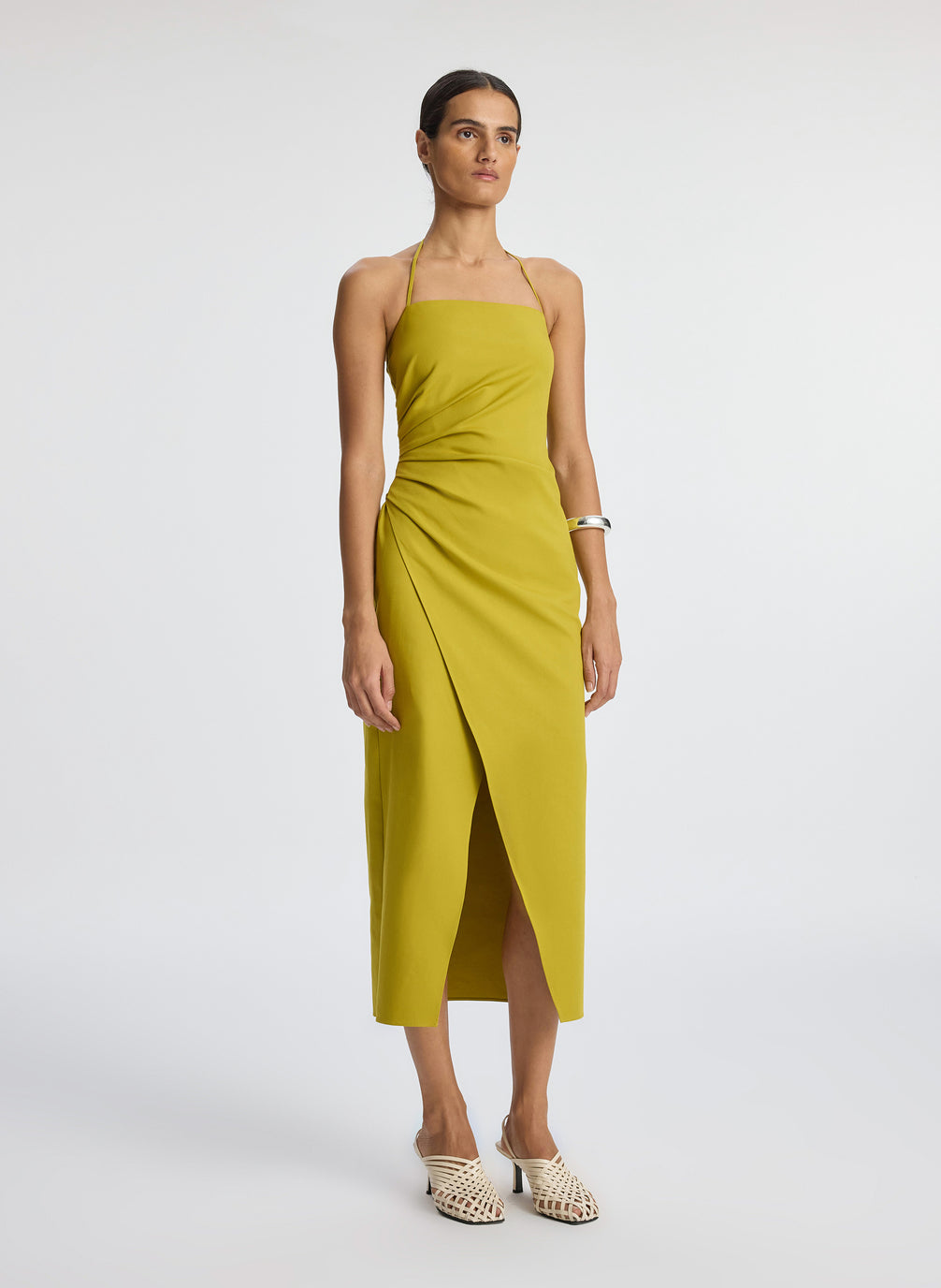 side  view of woman wearing yellow halter neckline ruched midi dress