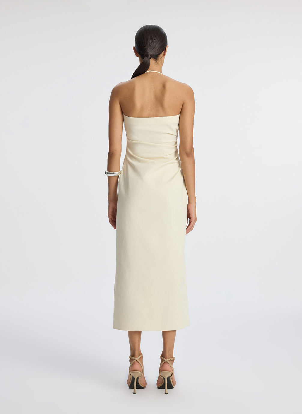 back view of woman wearing cream halter neckline ruched midi dress