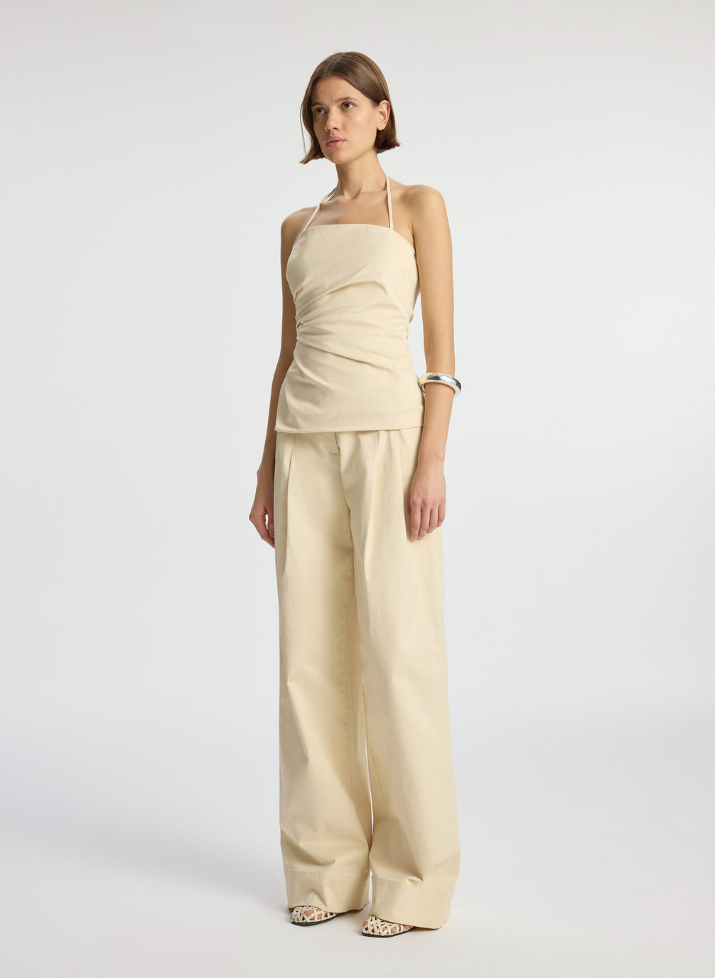 side  view of woman wearing beige halter top with side ruching and beige wide leg pant