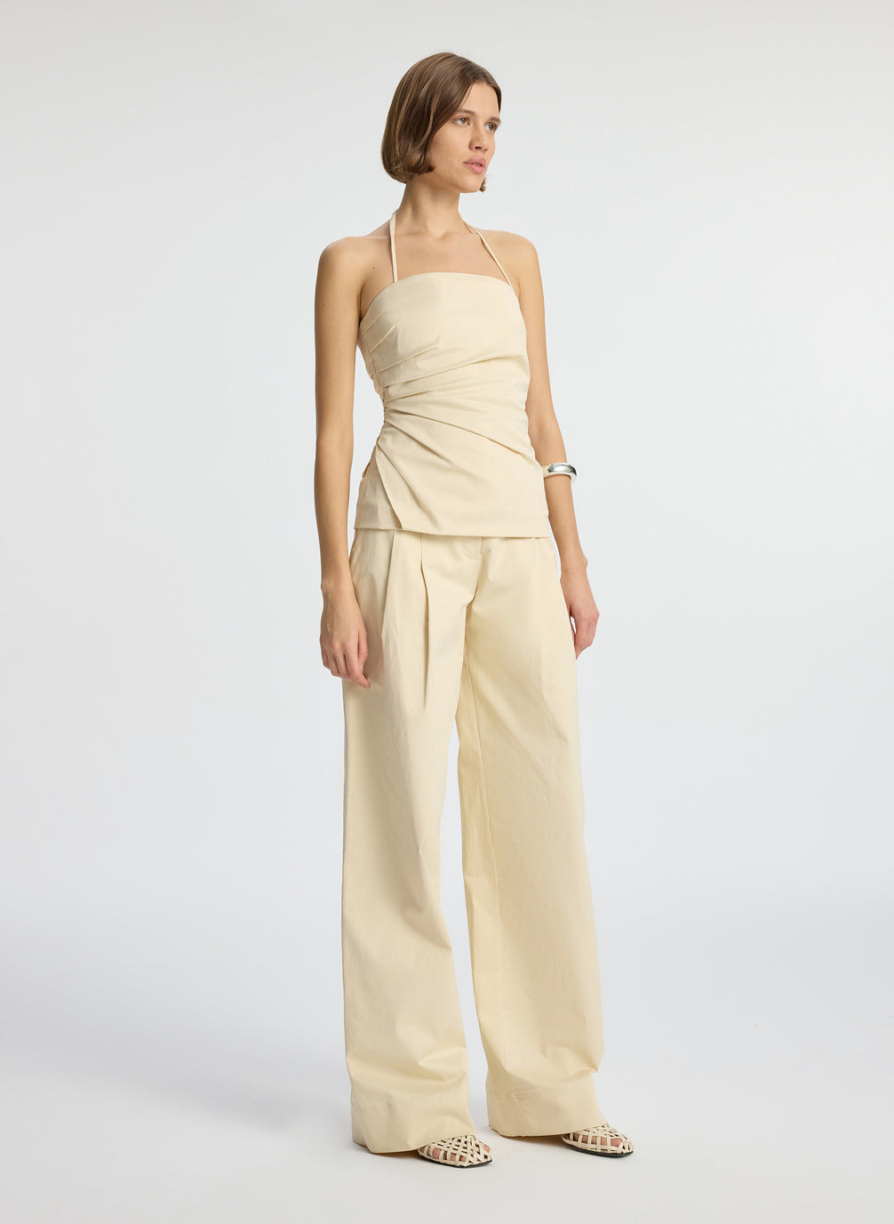 side  view of woman wearing beige halter top with side ruching and beige wide leg pant