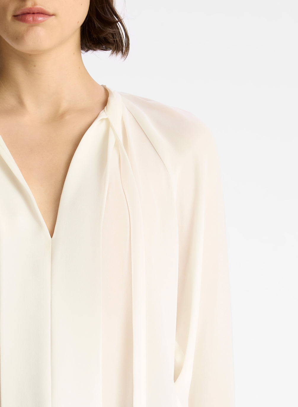 detail view of woman wearing cream long sleeve v neck blouse and navy blue pants