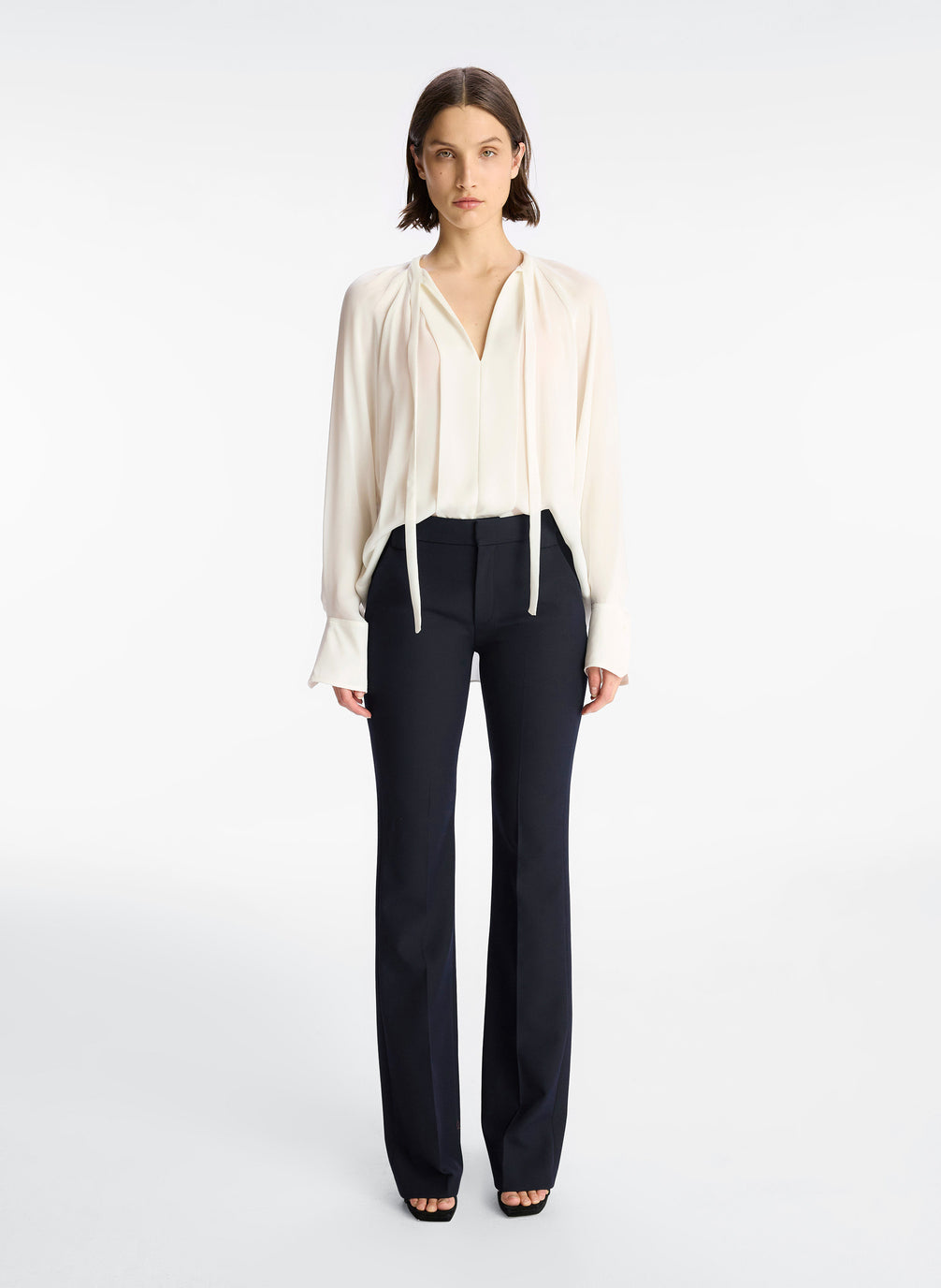 front view of woman wearing cream long sleeve v neck blouse and navy blue pants