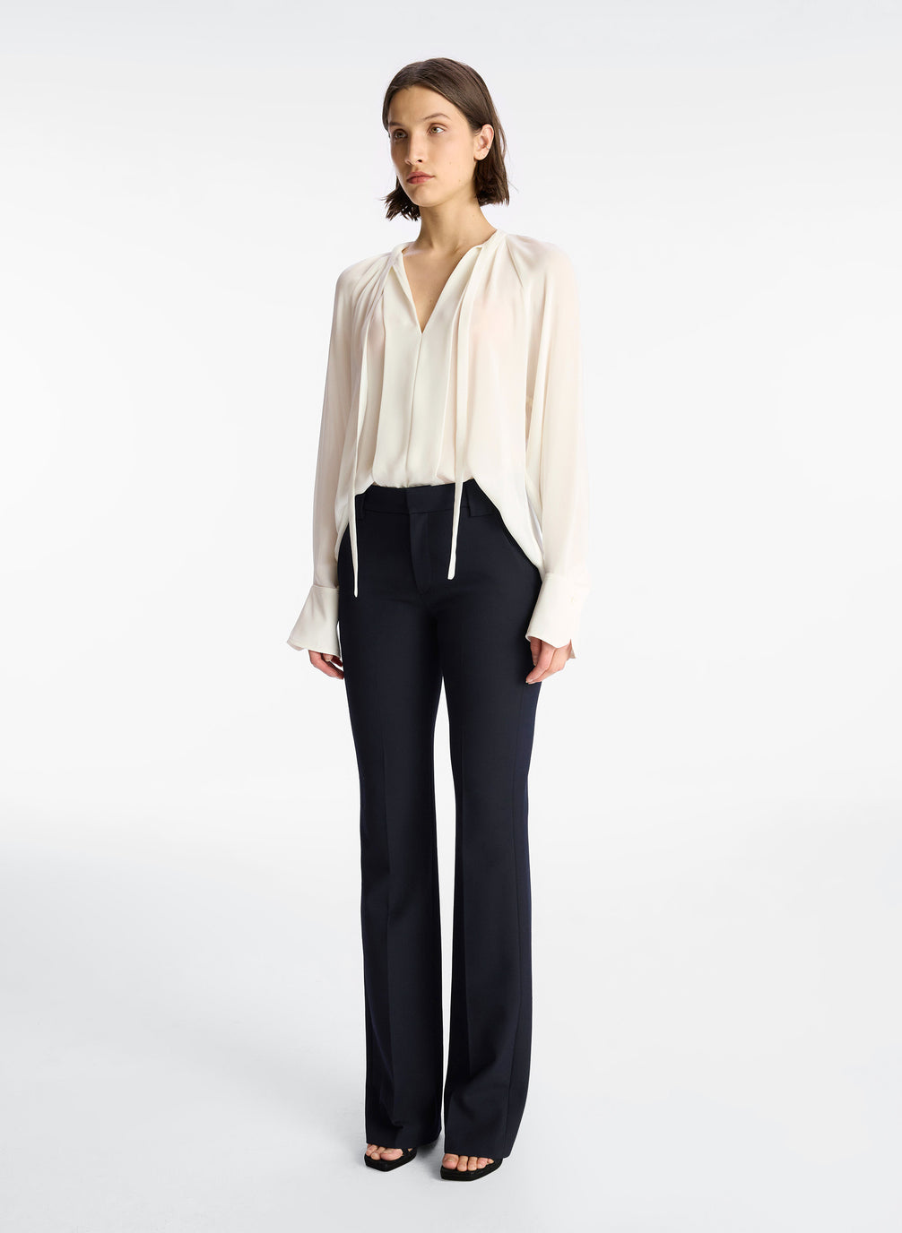 side view of woman wearing cream long sleeve v neck blouse and navy blue pants