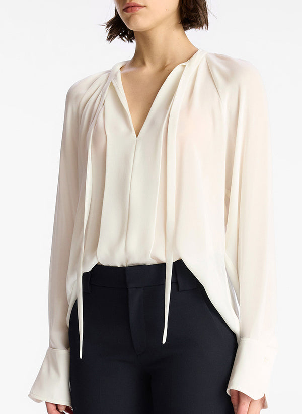 detail view of woman wearing cream long sleeve v neck blouse and navy blue pants