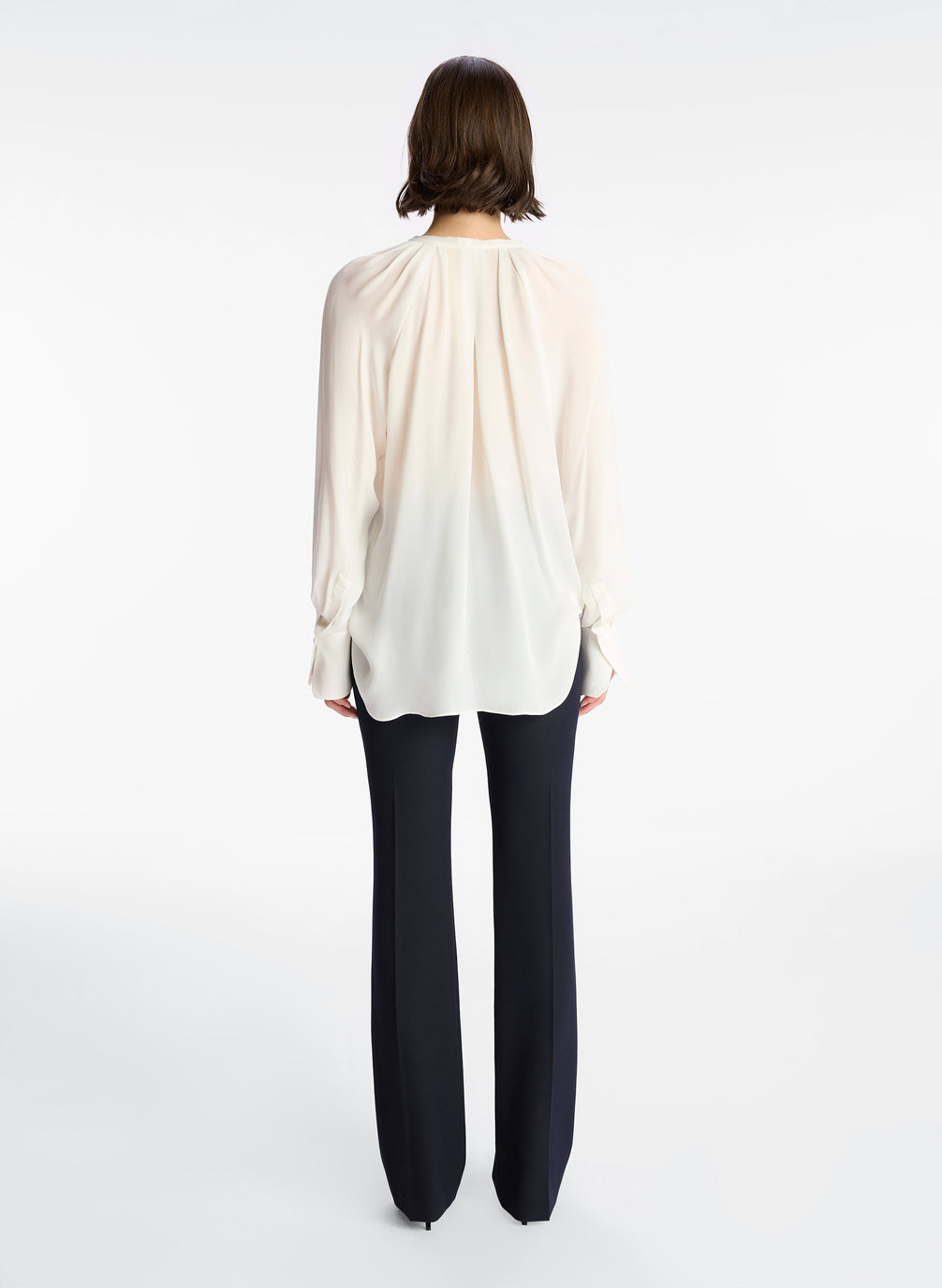 back view of woman wearing cream long sleeve v neck blouse and navy blue pants