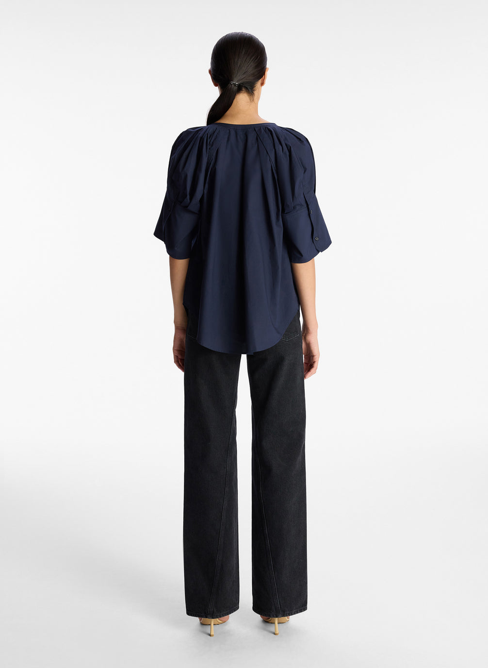back view of woman wearing navy blue wide sleeve blouse and dark denim jeans