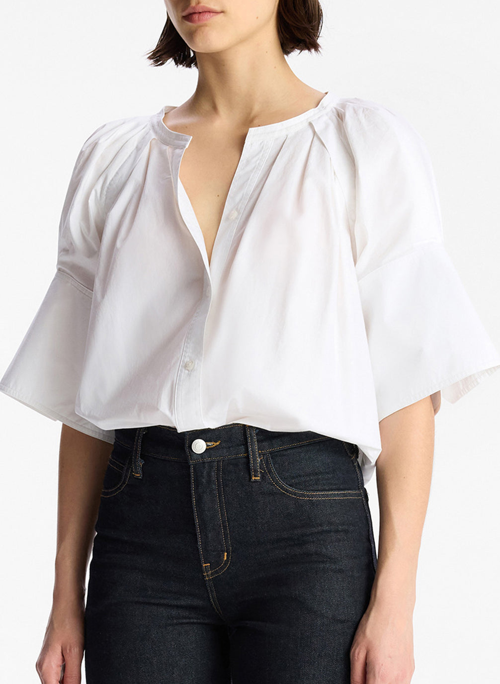 detail view of woman wearing white wide sleeve blouse and dark denim jeans