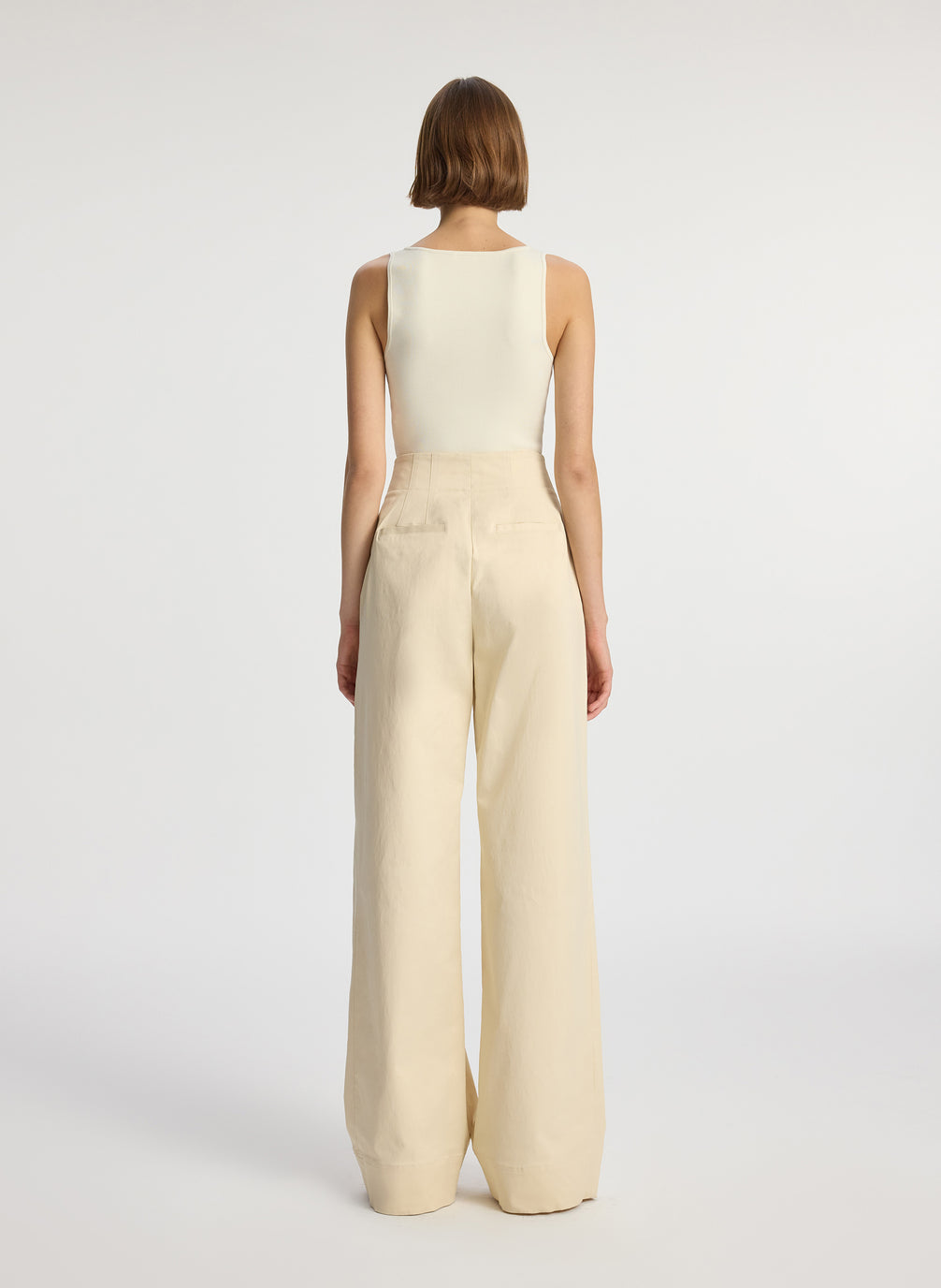 back view of woman wearing beige compact knit tank top and beige sateen wide leg pants