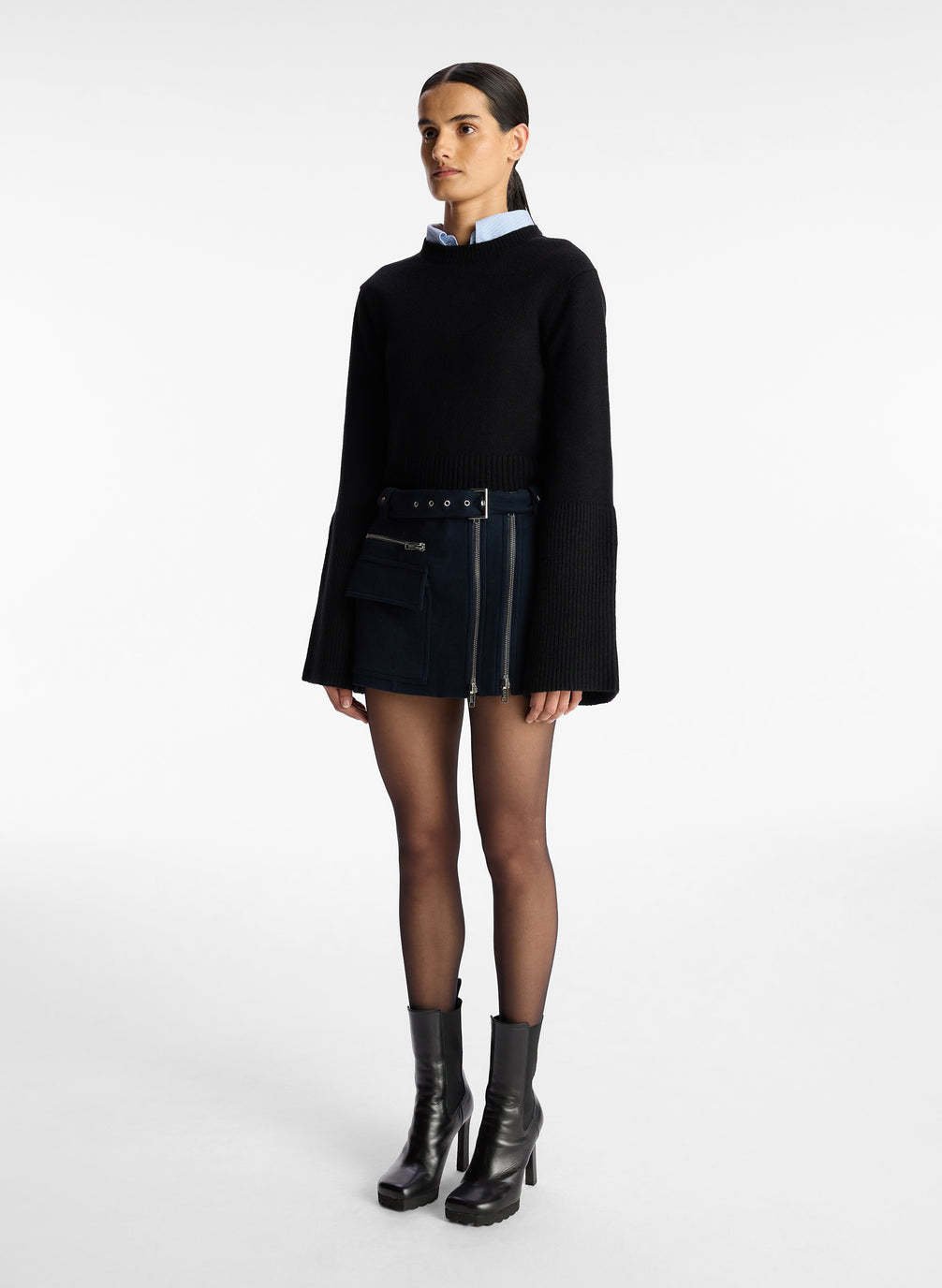 side view of woman wearing navy blue sweater, blue shirt, and navy zipper detailed mini skirt