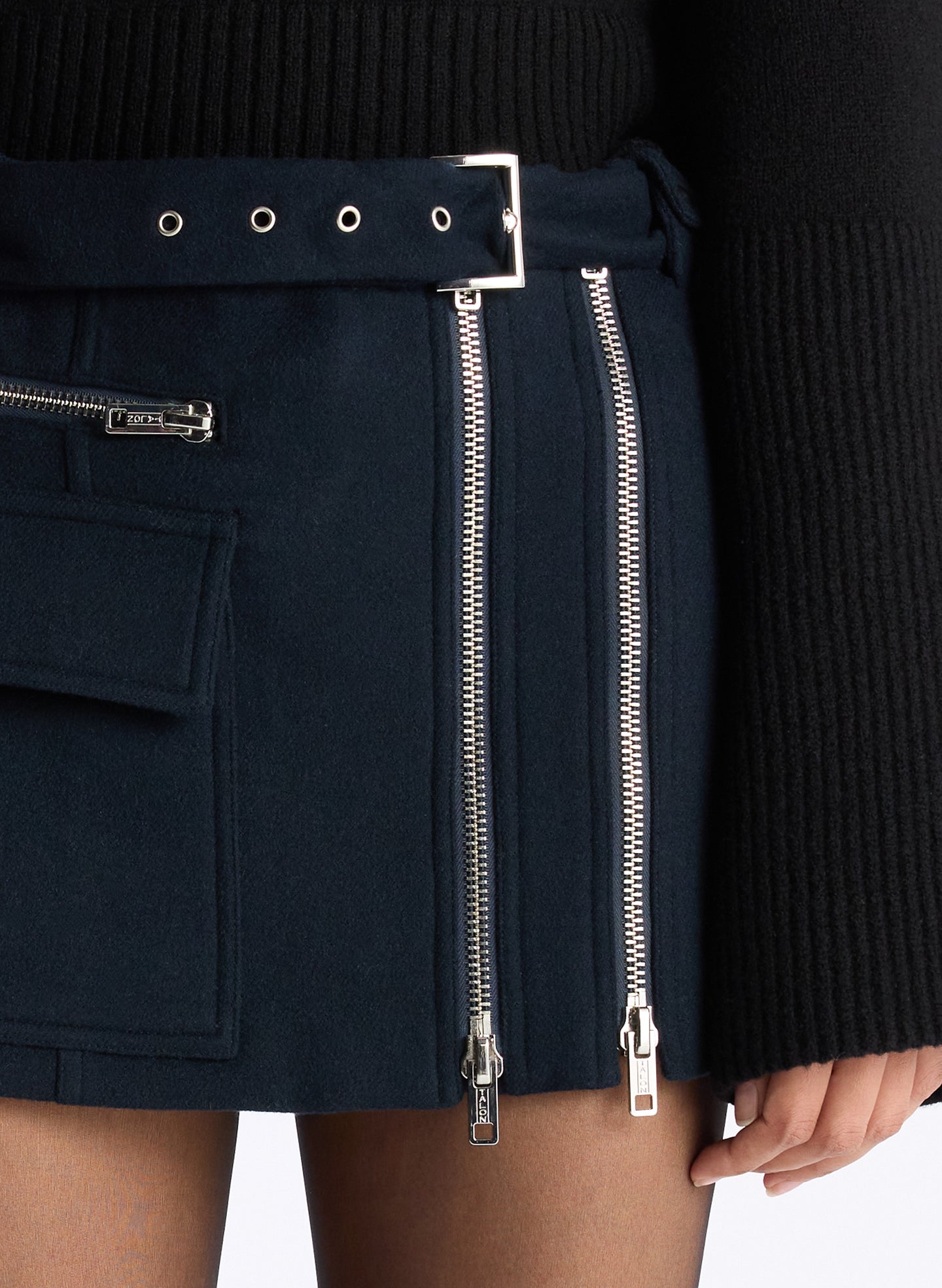 detail view of woman wearing navy blue sweater, blue shirt, and navy zipper detailed mini skirt