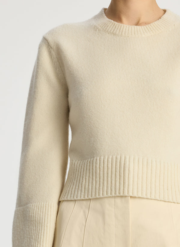 detail view of woman wearing cream sweater and beige pants