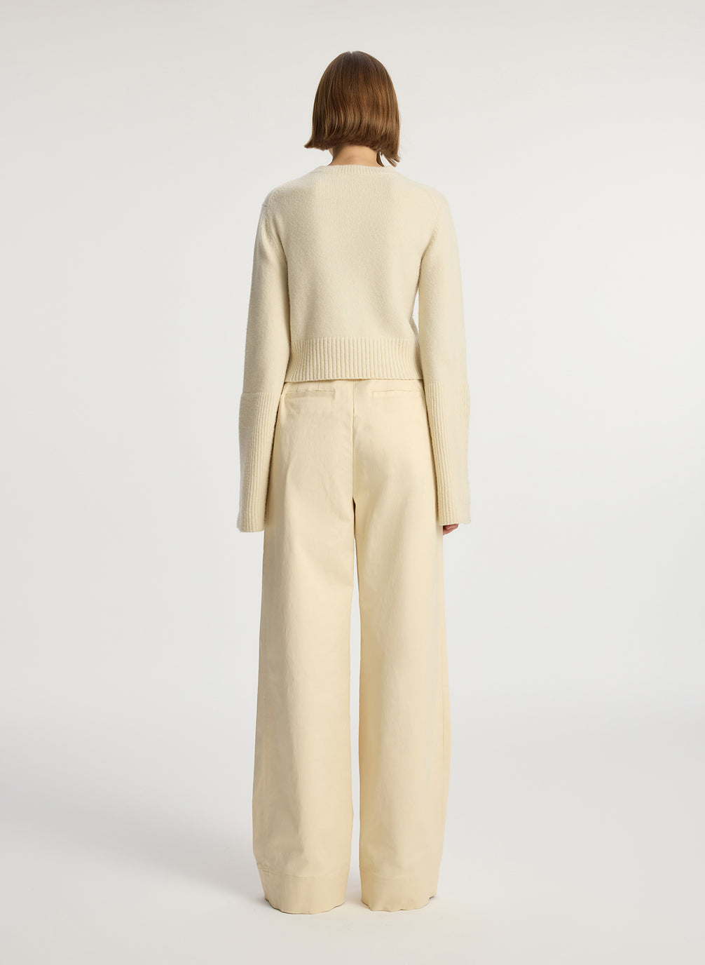 back view of woman wearing cream sweater and beige pants
