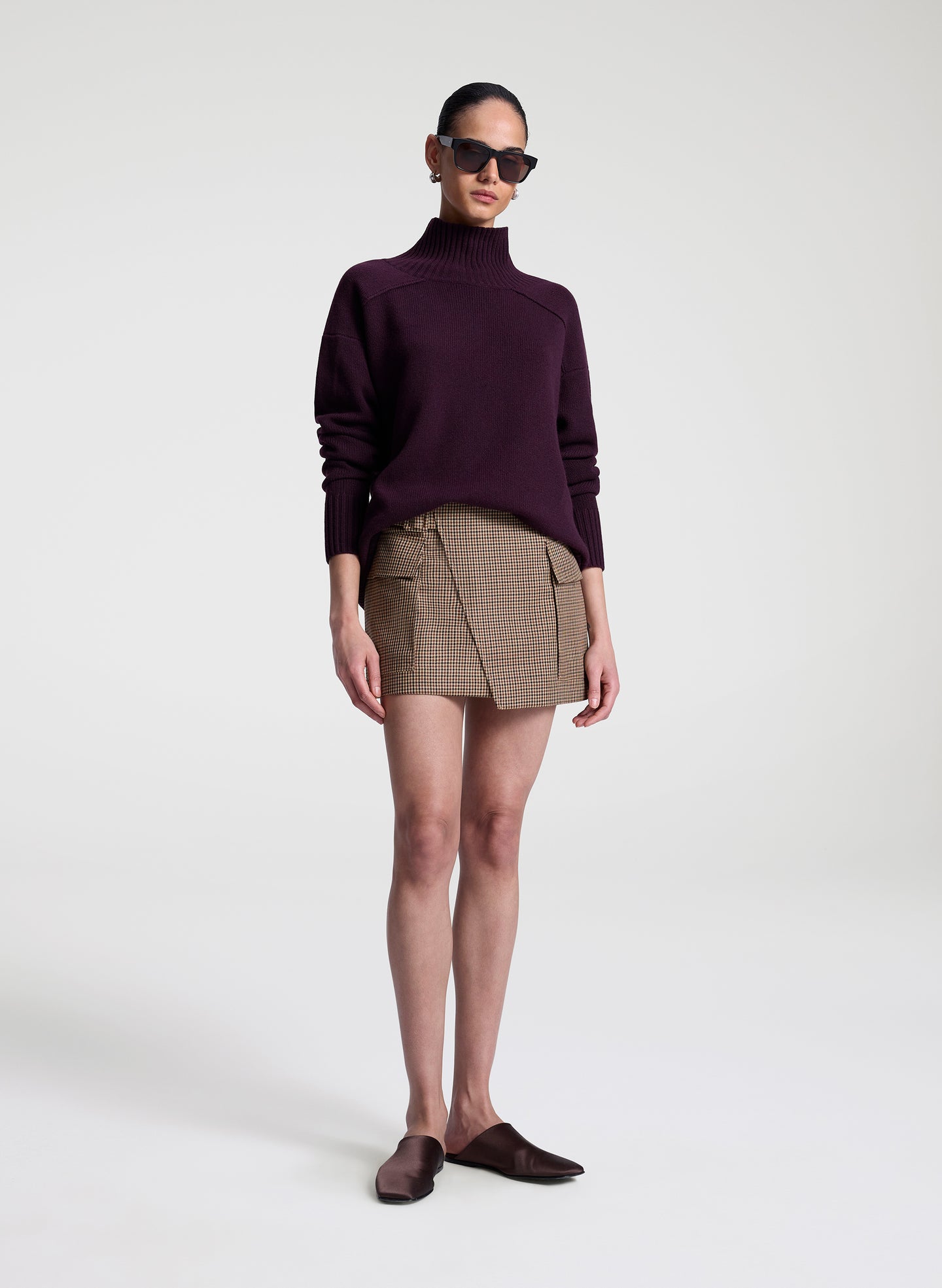 Person wearing a dark purple turtleneck sweater and plaid skirt on a white background
