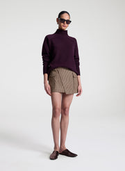 Person wearing a dark purple turtleneck sweater and plaid skirt on a white background
