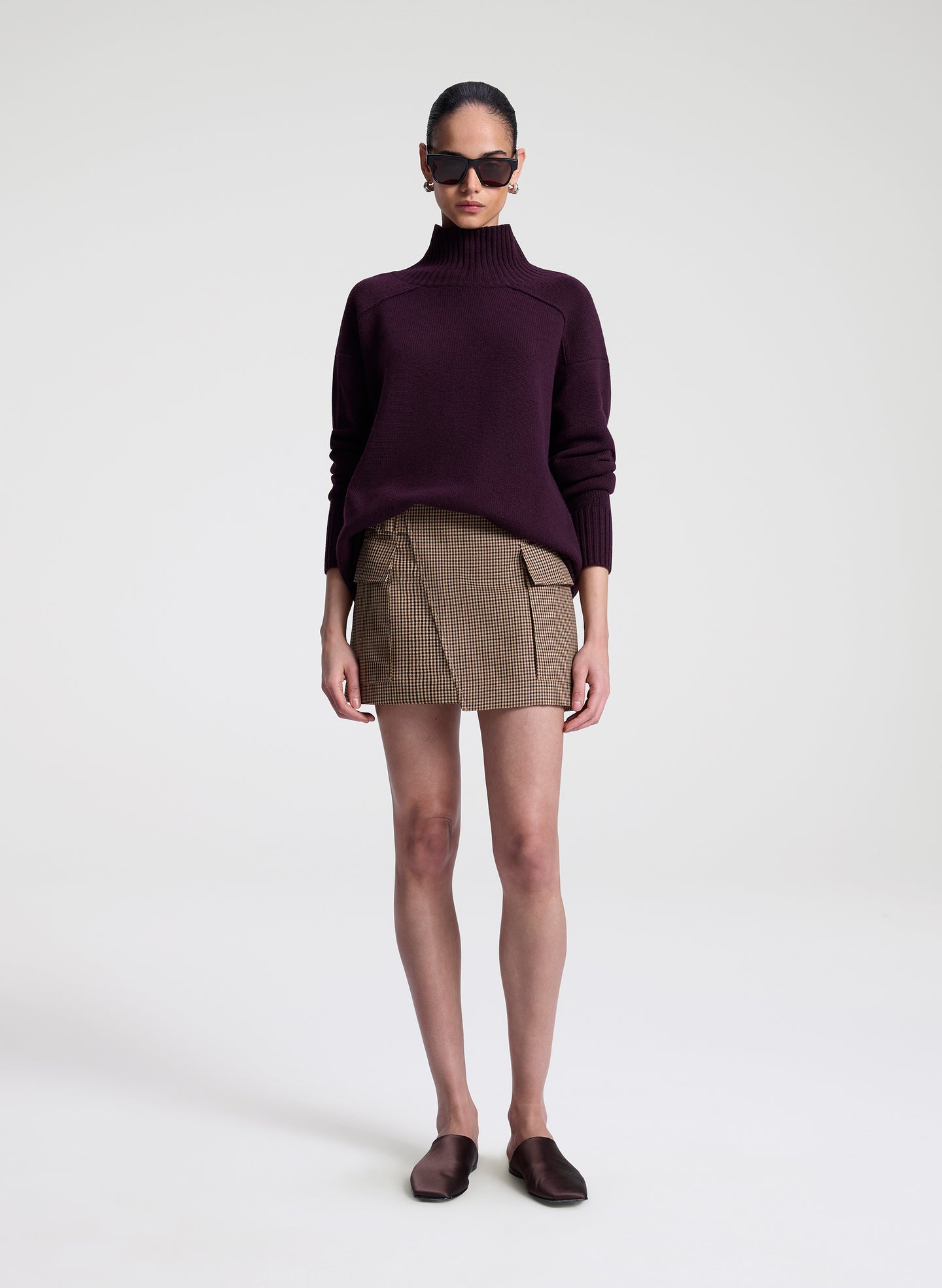 Person wearing a dark purple turtleneck sweater and patterned skirt on a white background