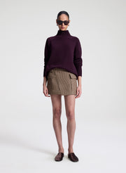 Person wearing a dark purple turtleneck sweater and patterned skirt on a white background