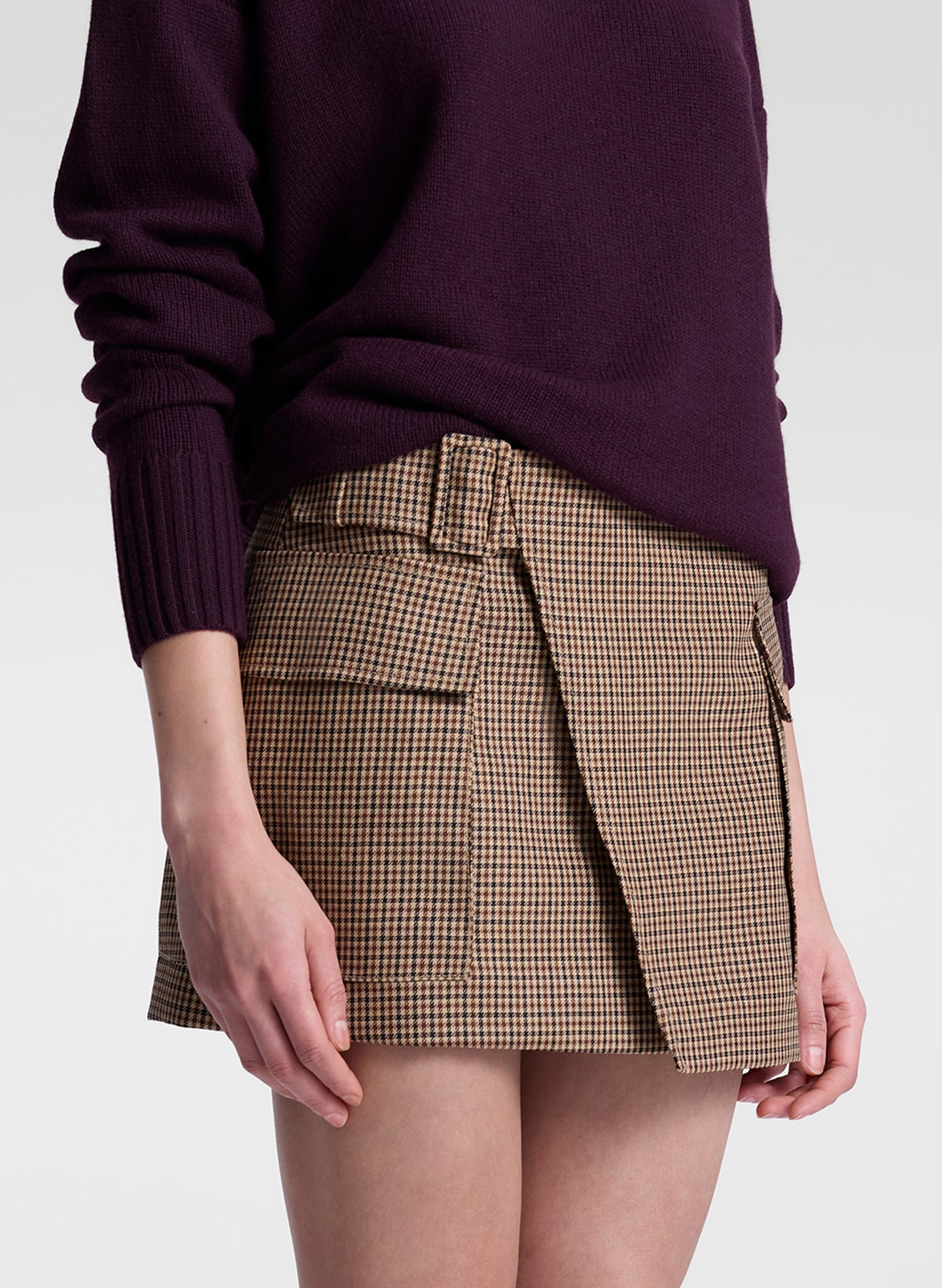 Person wearing a plaid skirt and dark sweater on a white background