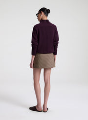 Person wearing a dark purple sweater and patterned skirt on a white background