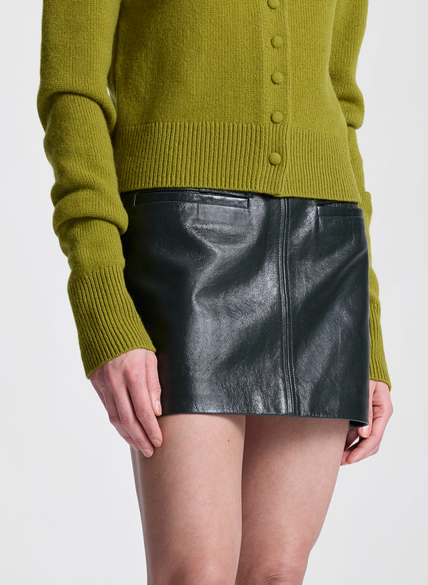 Woman wearing a green cardigan and green leather skirt on a white background