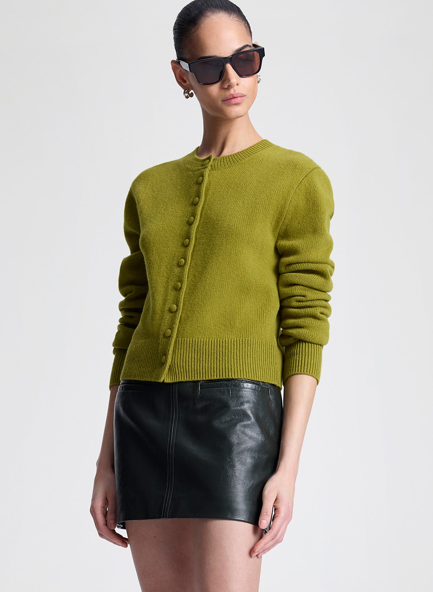 Woman wearing a green cardigan and green leather skirt on a white background