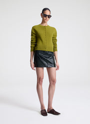 Woman wearing a green cardigan and green leather skirt on a white background