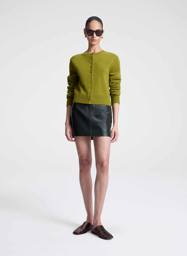 Woman wearing a green cardigan and green leather skirt on a white background