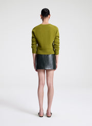 Woman wearing a green cardigan and green leather skirt on a white background