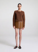 Woman wearing a brown cardigan and leather skirt on a white background
