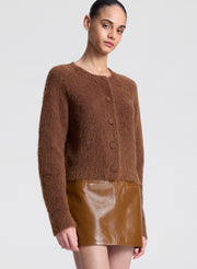 Woman wearing a brown knitted cardigan and leather skirt on a white background