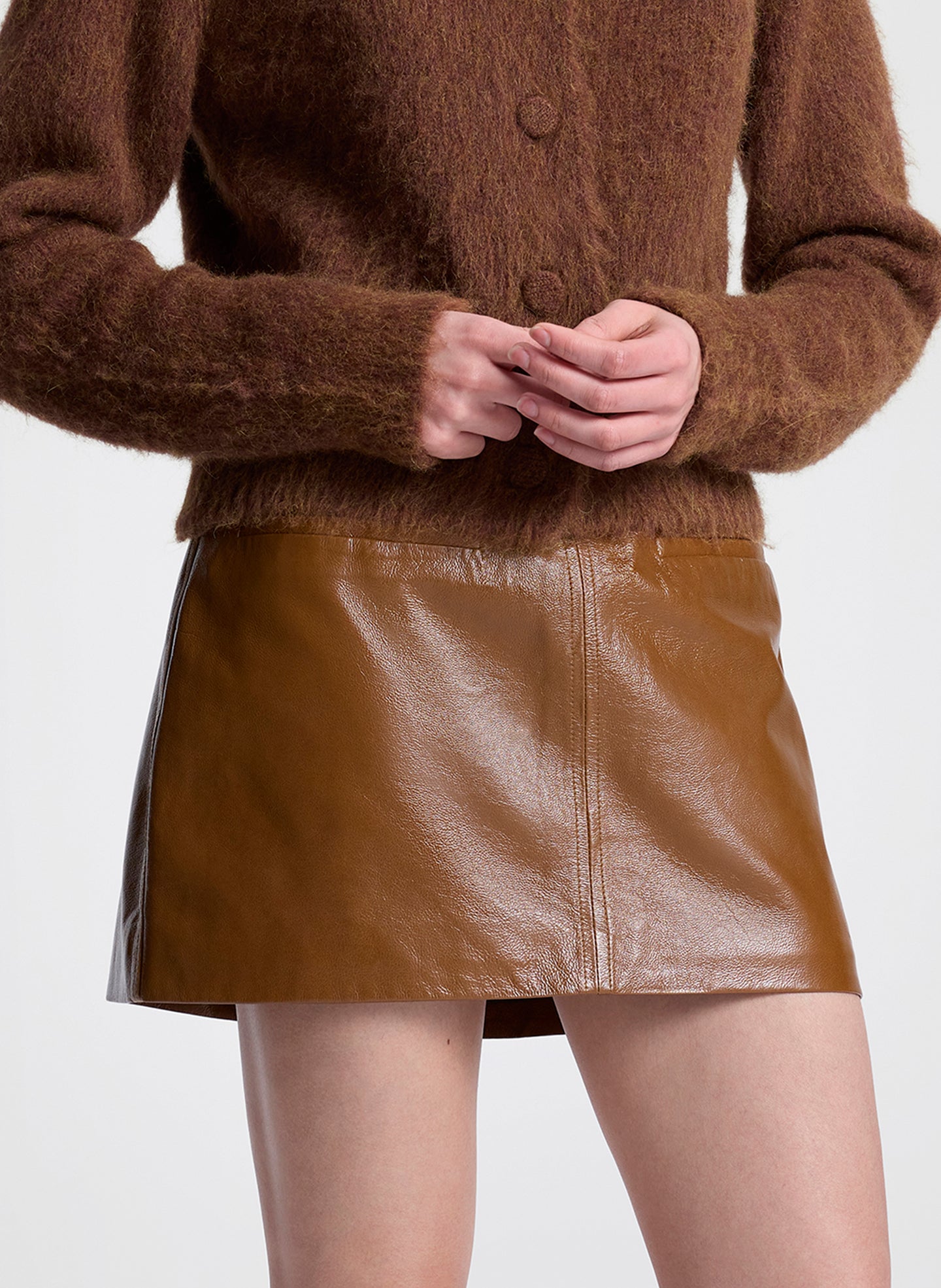 Brown cardigan and leather skirt on a plain background