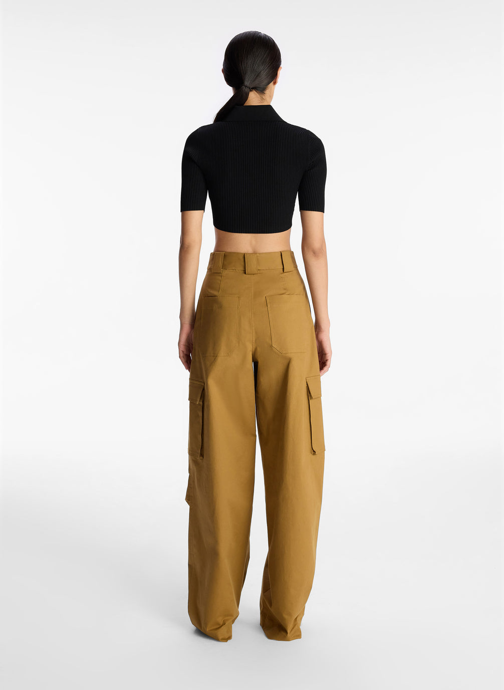back view of woman wearing black cropped collared knit shirt and tan cargo pants
