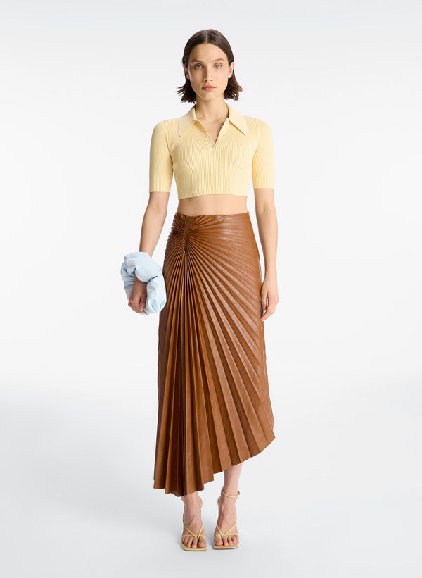 front view of woman wearing cream cropped collared knit shirt and brown pleated vegan leather skirt