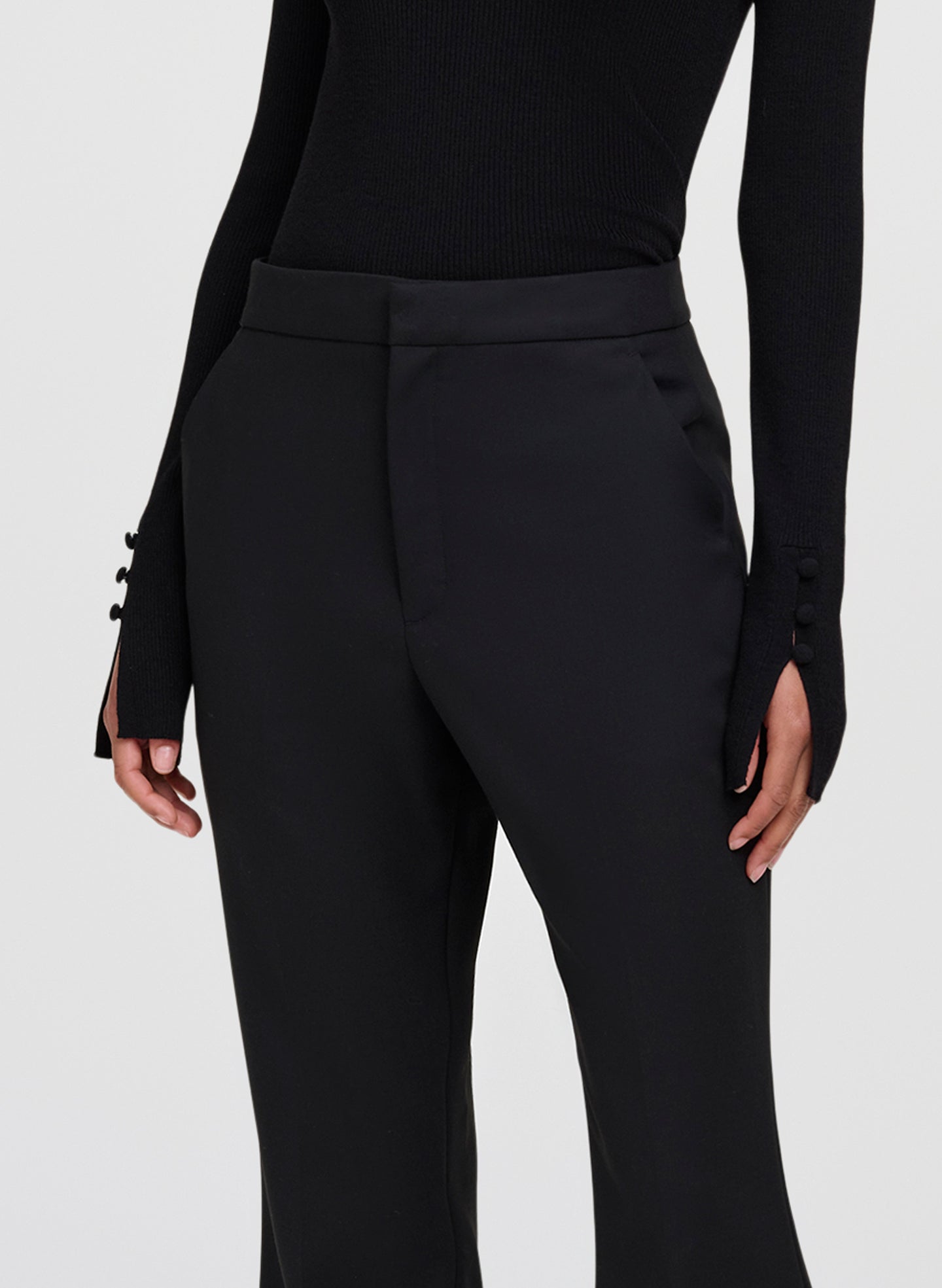 Black high-waisted trousers with a structured waistband and side buttons on the sleeves, shown on a model against a light gray background.