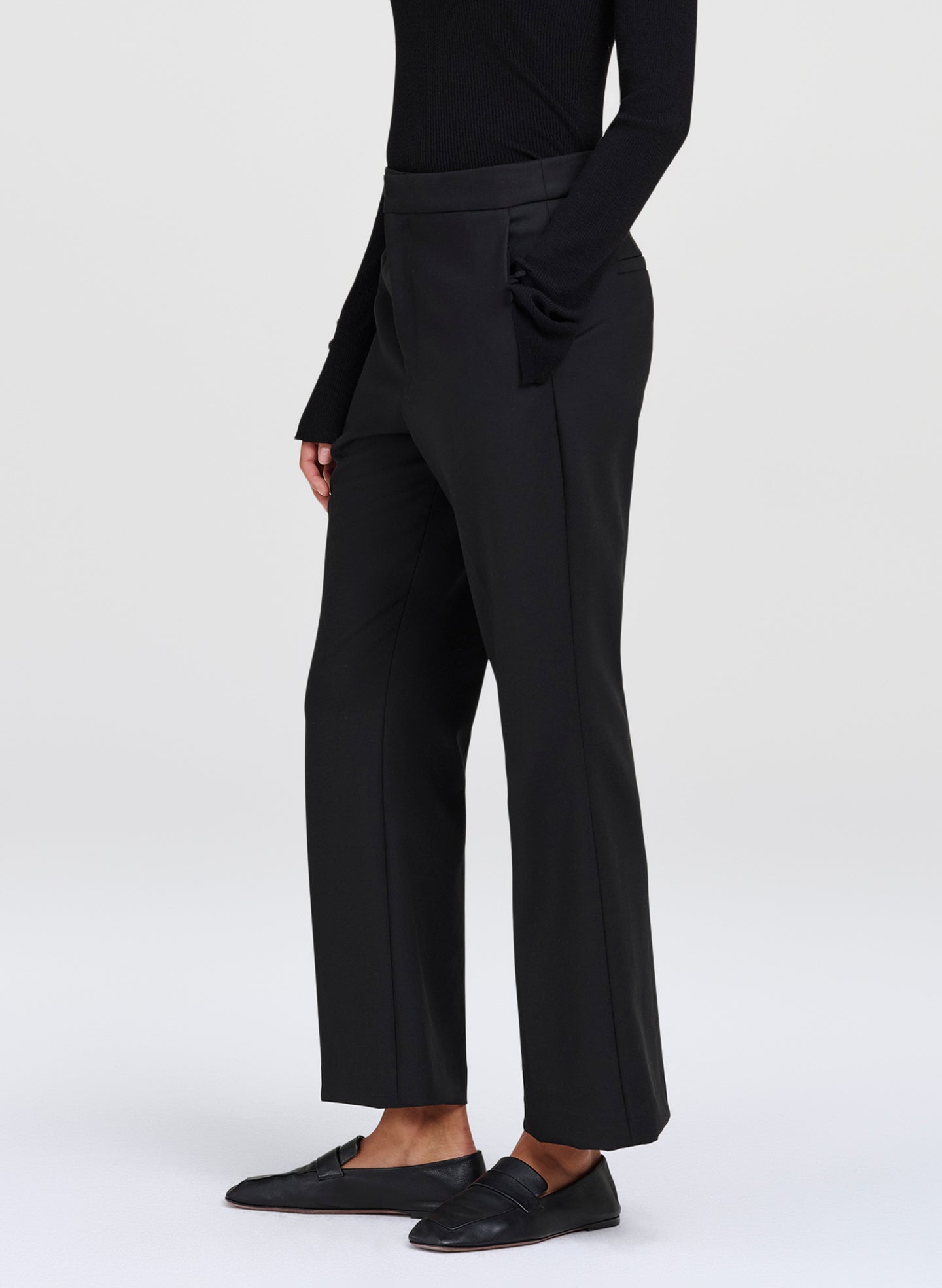 A model wearing black wide-leg cropped trousers, a black long-sleeve top, and black leather loafers, shown from the waist down against a light gray studio background.
