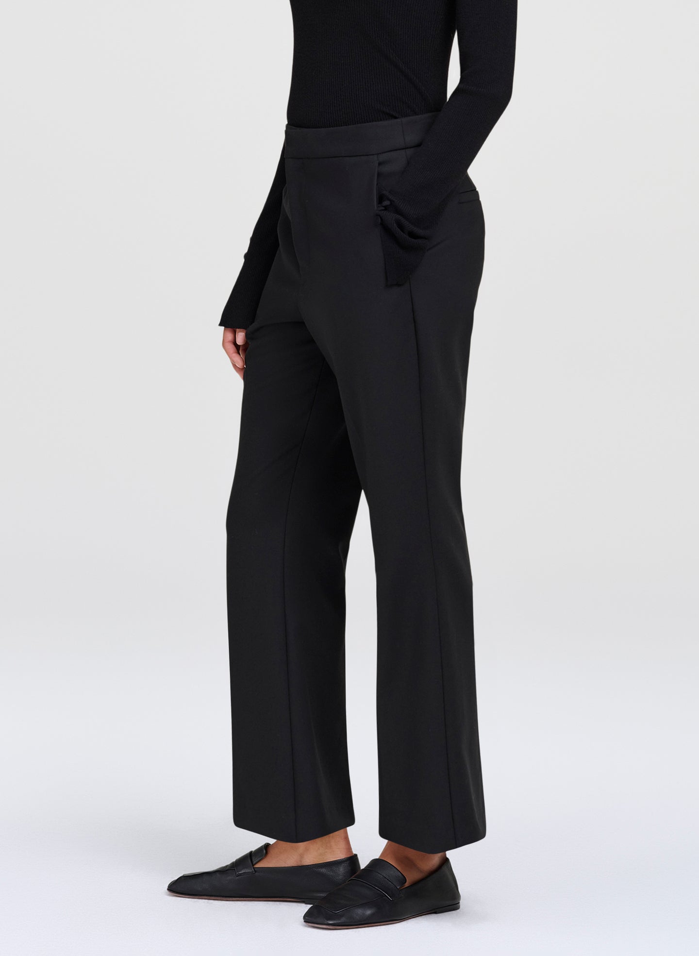 A model wearing black wide-leg cropped trousers, a black long-sleeve top, and black leather loafers, shown from the waist down against a light gray studio background.