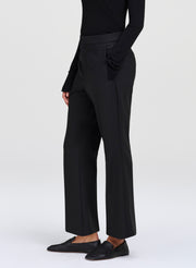 A model wearing black wide-leg cropped trousers, a black long-sleeve top, and black leather loafers, shown from the waist down against a light gray studio background.