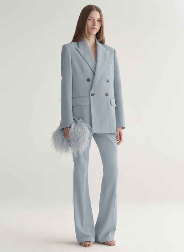 person wearing light blue suit carrying blue feathered handbag on a light gray background